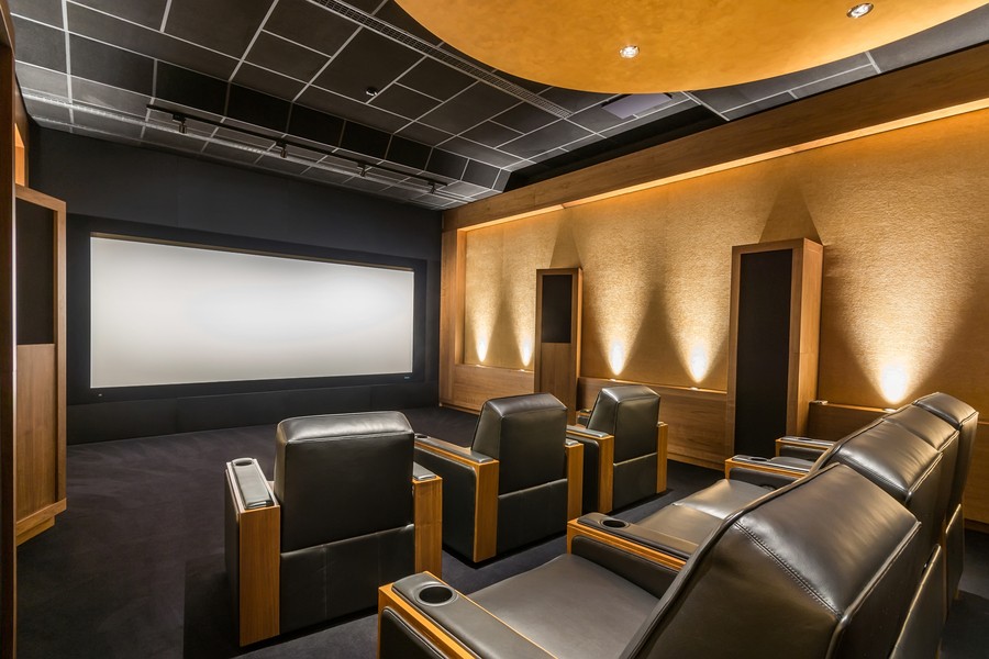 Media room with brown and beige tones, showing a blank screen and two rows of leather chairs. 