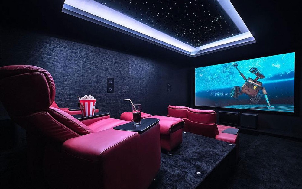 Dedicated home theater with rows of red recliner seats, a star ceiling and a large projector screen. 